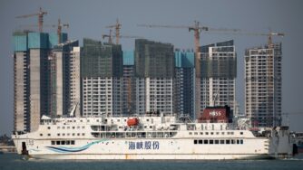 A ferry sails past residential buildings under construction on the waterfront in Haikou on Hainan island, China